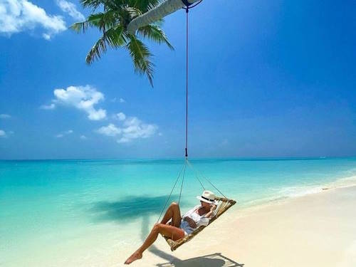 Woman relaxing on a swing tied to a palm tree over a pristine Maldives beach