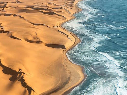 Aerial view of Namibia’s Skeleton Coast where golden sand dunes meet the ocean