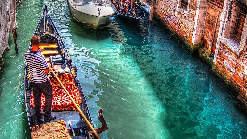 Gondolier navigating a gondola through the canals of Venice, Italy with tourists
